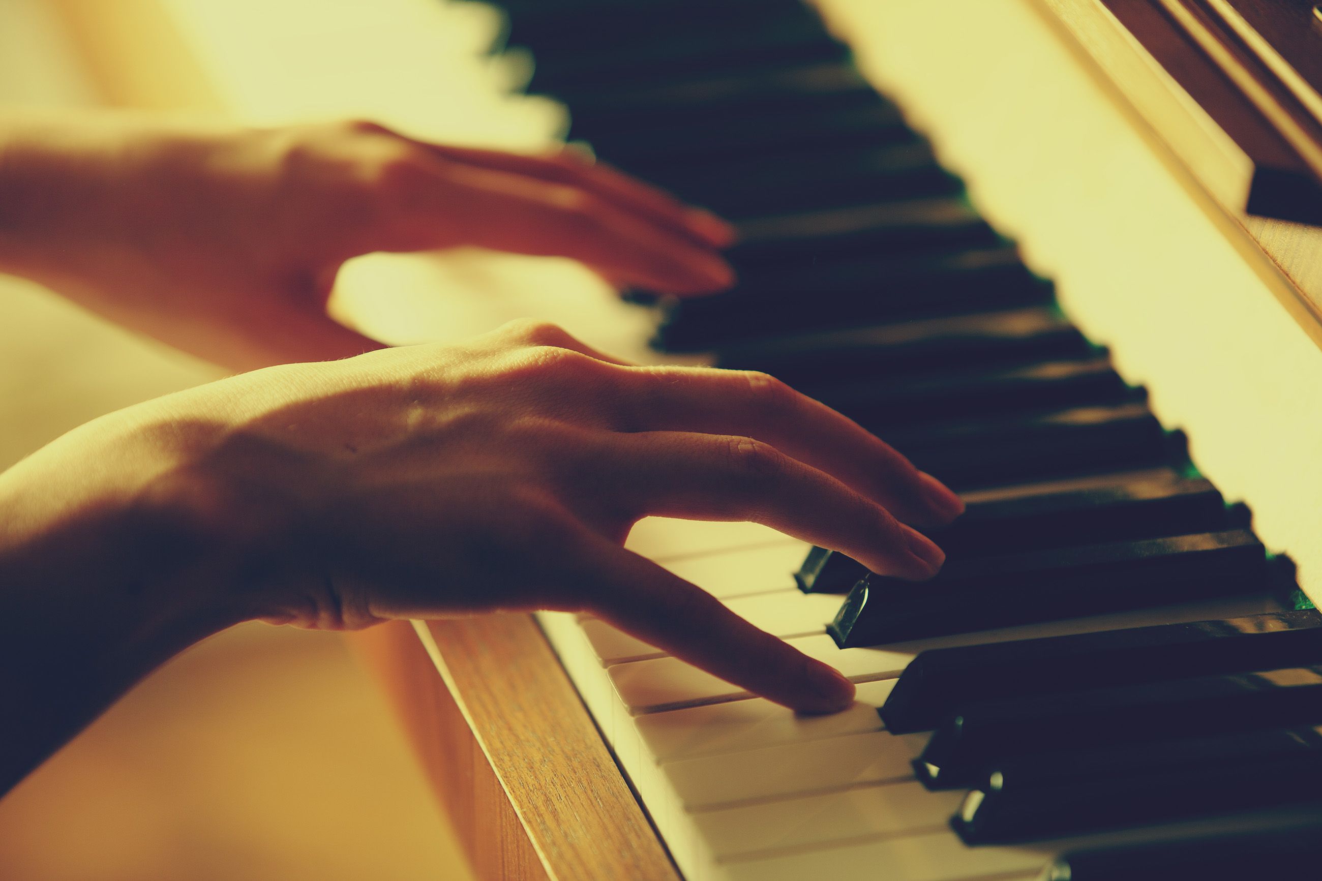 Hands playing a piano keyboard in warm light.
